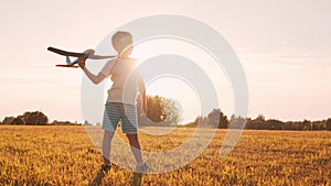 Boy plays with a toy plane in a field at sunset. The concept of childhood, freedom and inspiration.