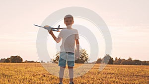 Boy plays with a toy plane in a field at sunset. The concept of childhood, freedom and inspiration.
