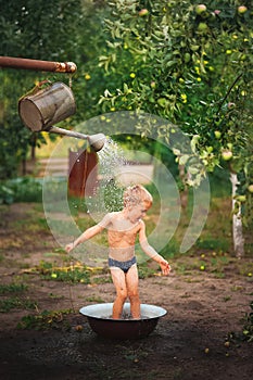 A boy plays with water close-up. The boy in the backyard drapes himself with water from a watering can and copy space