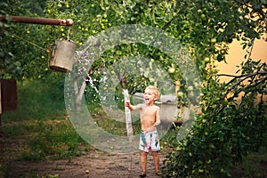 A boy plays with water close-up. The boy in the backyard drapes himself with water from a watering can and copy space