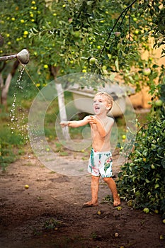 A boy plays with water close-up. The boy in the backyard drapes himself with water from a watering can and copy space