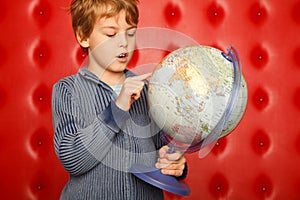 Boy pointing finger on globe. Portrait on red