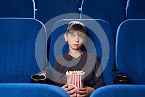 Boy with poker face watching boring film in cinema