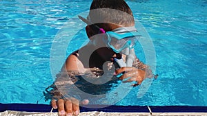 A boy in the pool with a mask and goggles holds on to the edge and dives into the pool.