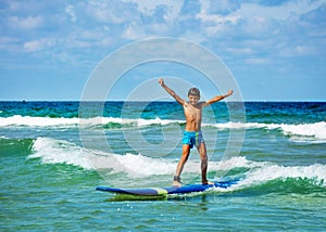 Boy pose with lifted hands ride surfboard on wave