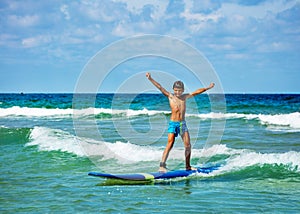 Boy pose with lifted hands ride surfboard on wave photo