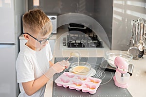 Boy pouring muffin dough into molds. Child coocking cupcakes.