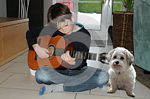 Boy practicing playing guitar, his dog listens to the music