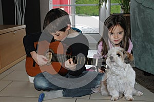 Boy practicing playing guitar, his sister listens to the music