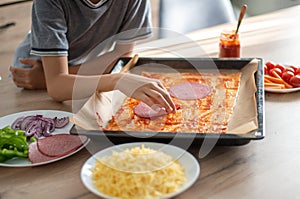 A boy preparing dinner making pizza on wooden table at home for dinner focus on hand
