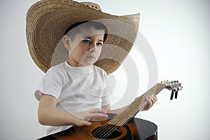 boy of preschool age in hands with guitar in large Mexican hat sits on white background looks thoughtfully invents