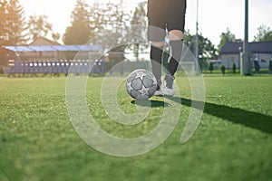 A boy in a professional uniform and cleats runs after a soccer ball making a pass on a football field with artificial grass floori