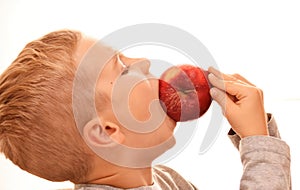 Boy in profile bites a whole red apple