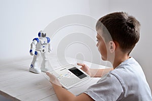 Boy is programming the work of a robot on a desk with a tablet in his hand