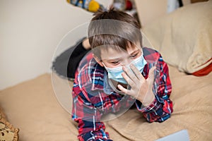 Boy in protectiv medical mask does lessons on laptop. child learns remotely during quarantine of coronavirus. Online learning from