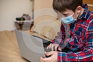 Boy in protectiv medical mask does lessons on laptop. child learns remotely during quarantine of coronavirus. Online learning from