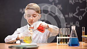 Boy in protective glasses mixing chemical liquids in flasks, curious genius