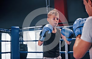 Boy in protective gloves have sparring with trainer on the boxing ring
