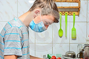 A boy in a protective mask is preparing food in the kitchen at home, quarantined during the covid-19 pandemic