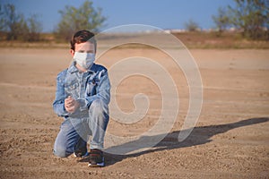 Boy in protective medical mask is sitting on the ground, upset and depressed