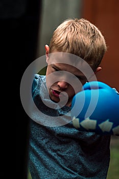 A boy punches a punching bag in blue gloves in the yard