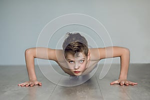 The boy is pushing up from the floor at home. Quarantine and sport concept. The child develops willpower and mode