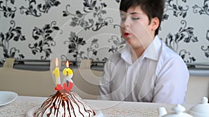 The boy puts out the candles on cake with numbers 13