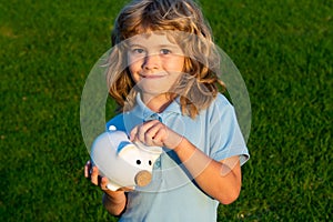 Boy putting money into a piggy bank. Portrait of a joyful cute little kid holding saving piggybank.