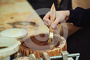 Boy is putting a protective mordant on the wooden disk, closeup. Young carpenter working with wood in craft workshop