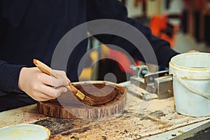 Boy is putting a protective mordant on the wooden disk, closeup. Young carpenter working with wood in craft workshop