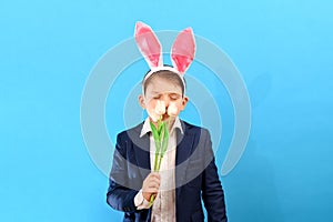 A boy with rabbit ears holds tulips in his hand and sniffs them