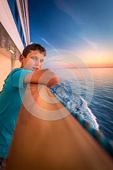 Boy at the railing of a cruise ship at sunset.