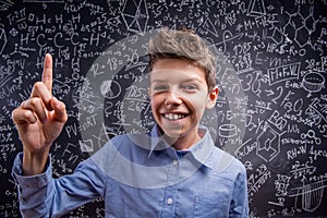 Boy with raised finger against big blackboard with formulas