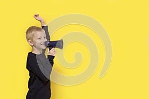 boy with a raised hand with a smile shouts into a bullhorn on a yellow background with copy space