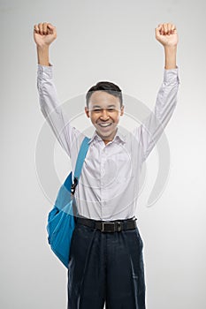 a boy raised hands in junior high school uniform smiling with school bag