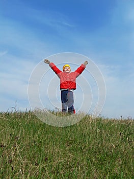 The boy is raising his hands against the blue sky