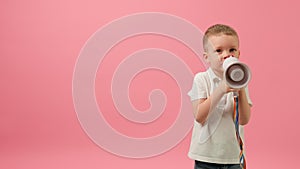 Boy rallies with loudspeaker on pink background. Blond caucasian 5-year-old child in white T-shirt shouts into megaphone