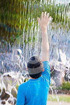 Boy reaching up to feel water in a waterfall