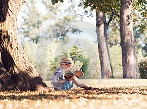 Boy read a book in tree shadow in sunny day