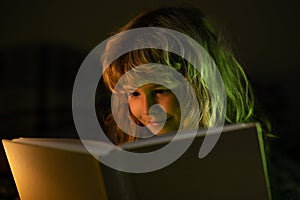 Boy reading bedtime story, dark room photo. Child reading a magic book in bed. Kid boy read books at home.