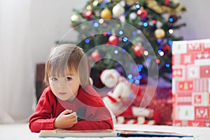 Boy, reading a book in front of a Christmas tree.