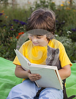 Boy reading book with kitten in the yard, child with pet reading