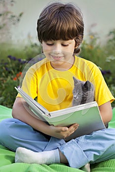 Boy reading book with kitten in the yard, child with pet reading