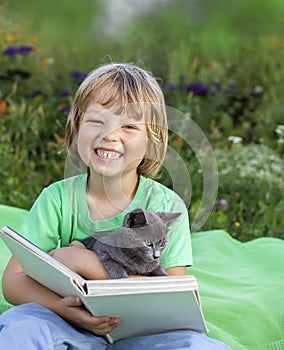 Boy reading book with kitten in the yard, child with pet reading