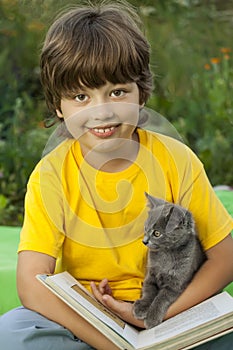 Boy reading book with kitten in the yard, child with pet reading