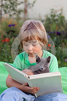 Boy reading book with kitten in the yard, child with pet reading