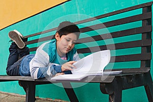 Boy reading and turning the page of a book lying on a bench