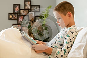 The boy reads a book at home. Before going to bed, the student lies in bed and studies the encyclopedia