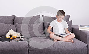 Boy reads an interesting book of the sofa.