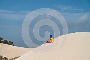 Boy is ready for sliding down the sand dune on sandboard